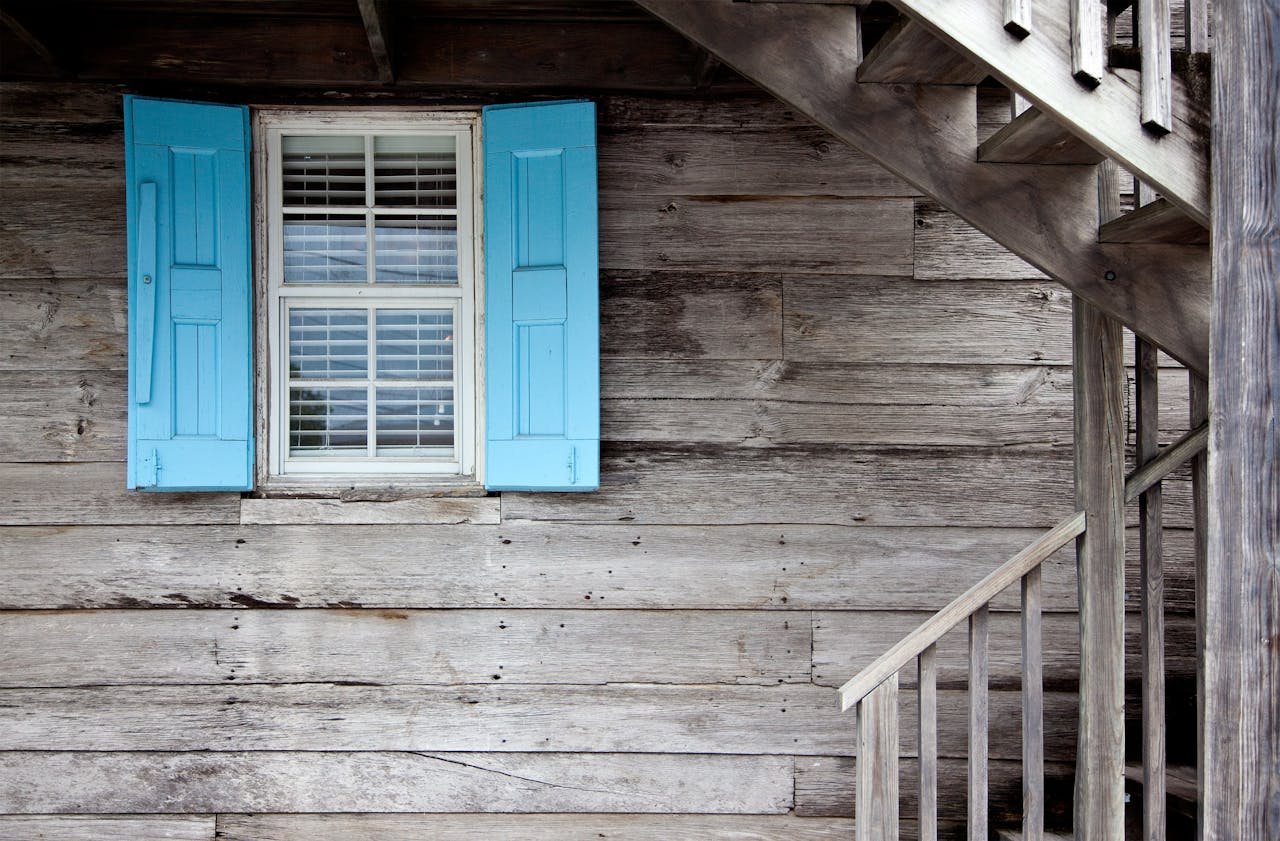 A rustic wooden cabin exterior with blue shutters and an outdoor staircase, showcasing simplicity and warmth.